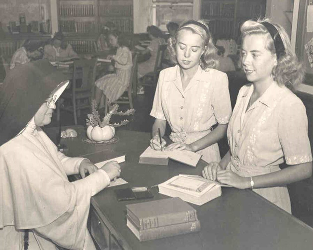 Sister Michael James Carter, O.P. checks out books to twin sisters Grace Ann and Janith Schaefer in the library